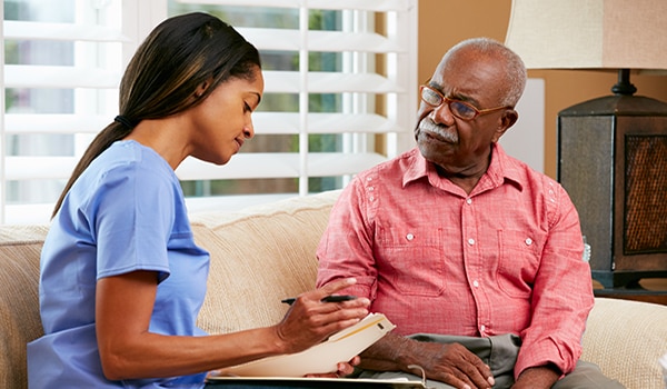 Image of a young female doctor sitting on a couch looking over paperwork with an older male patient.