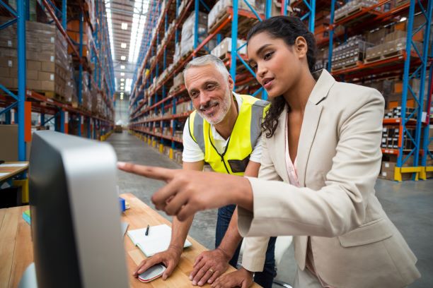 Male and female coworkers look at a computer screen while in a warehouse.