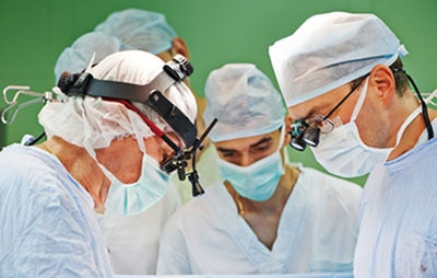 Surgeons with surgical caps, masks, and gowns looking down during surgery.