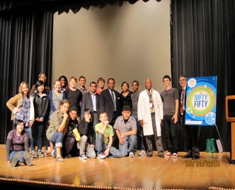 Scientists and students stand on a stage, smiling toward the camera.