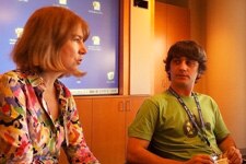 A woman on the left talks with a teenage boy. Both sit at a table in a conference