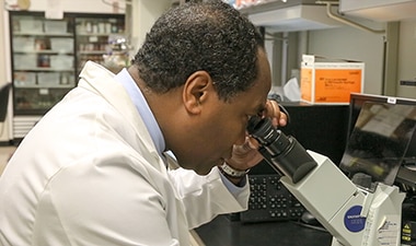 Photo of Dr. Griffin P. Rodgers looking through a microscope