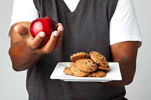 Photo of an apple in one hand and a plate of cookies in the other hand