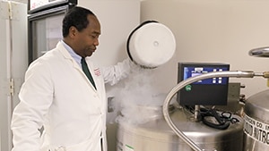 Photo of Dr. Griffin P. Rodgers in labcoat observing liquid nitrogen tank.