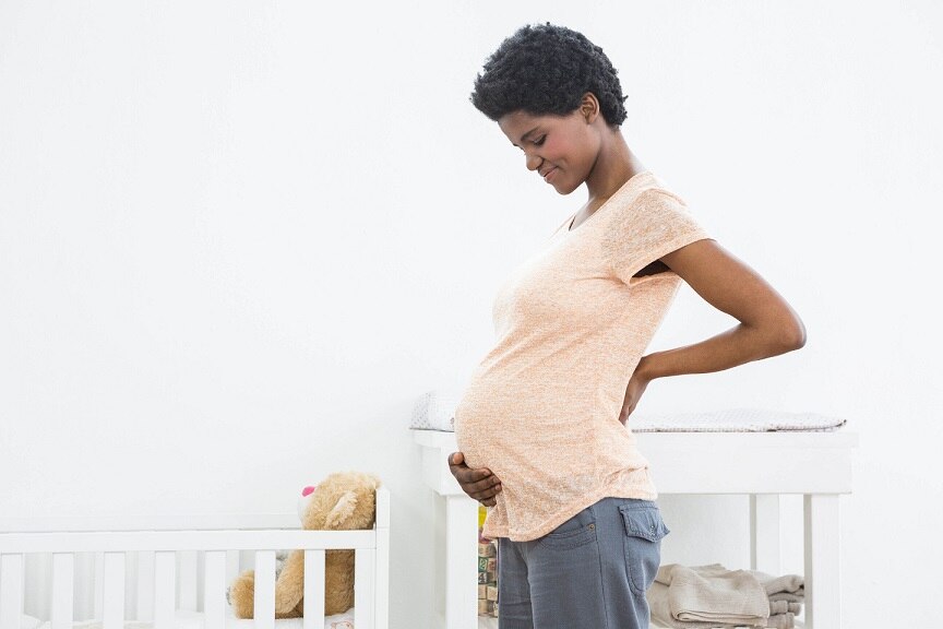 Photo of a pregnant woman next to a crib.