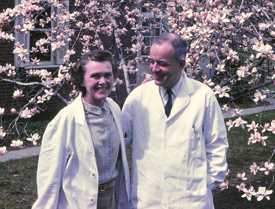 Herbert Tabor and Celia in lab coat in front of a blooming tree.