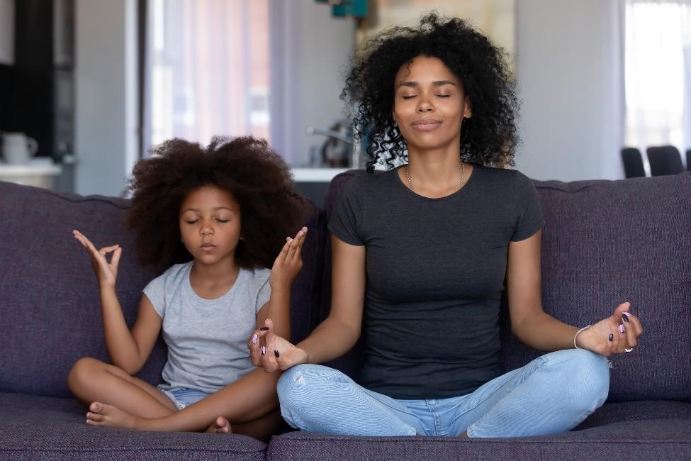 A woman and her child meditating on the sofa.