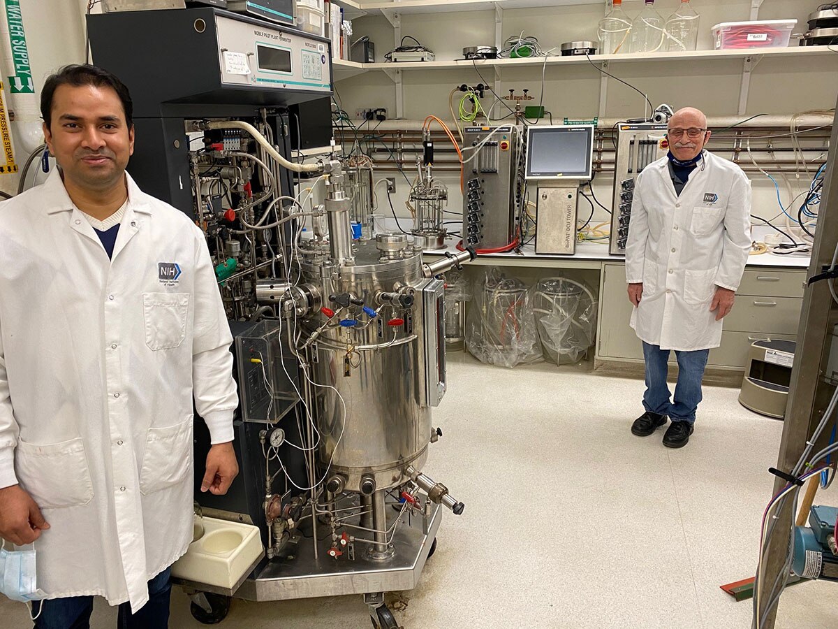 Two male scientists standing next to a bioreactor tank in their lab