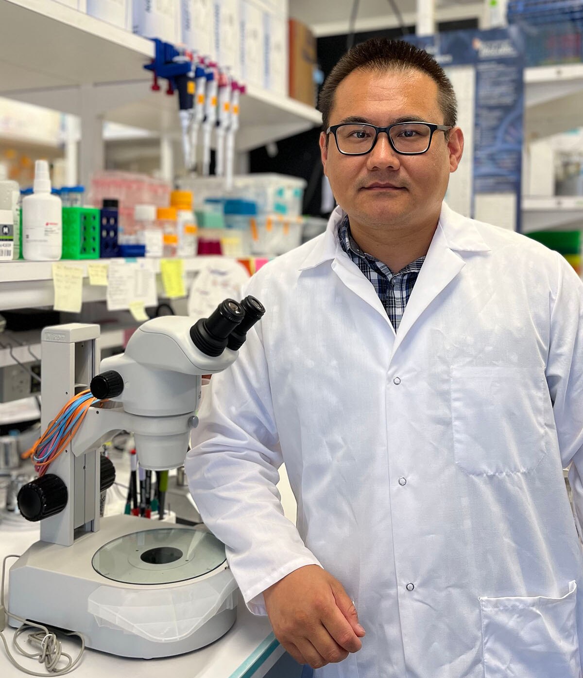 Dr. Xiaofei Bai standing next to a microscope in the lab