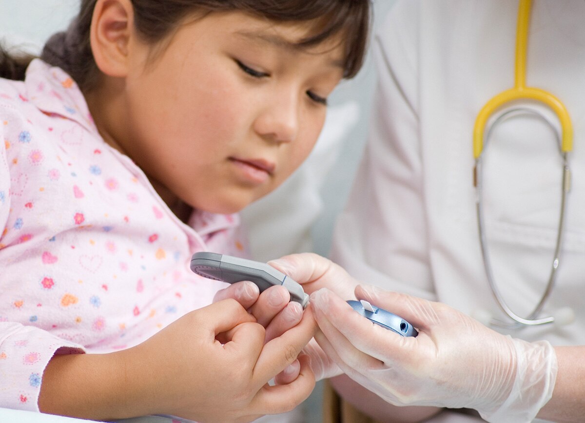 A health care professional pricking a girl's finger with a lancet to test her blood glucose level.