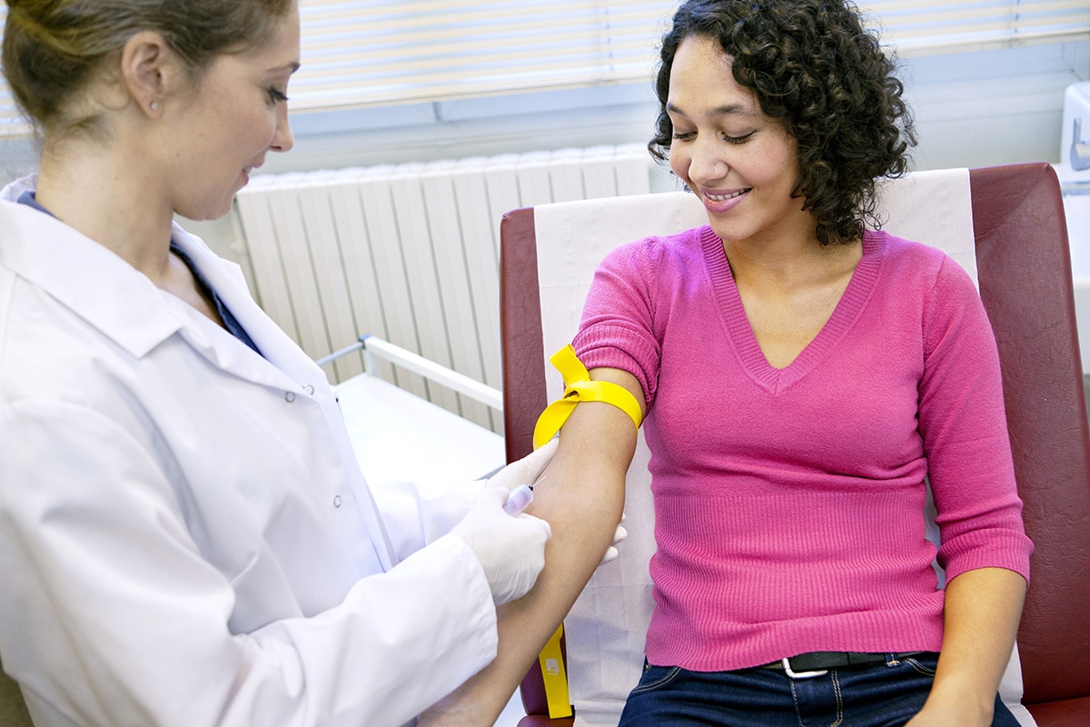 Woman health care professional holding the arm of a woman sitting on an exam bed.
