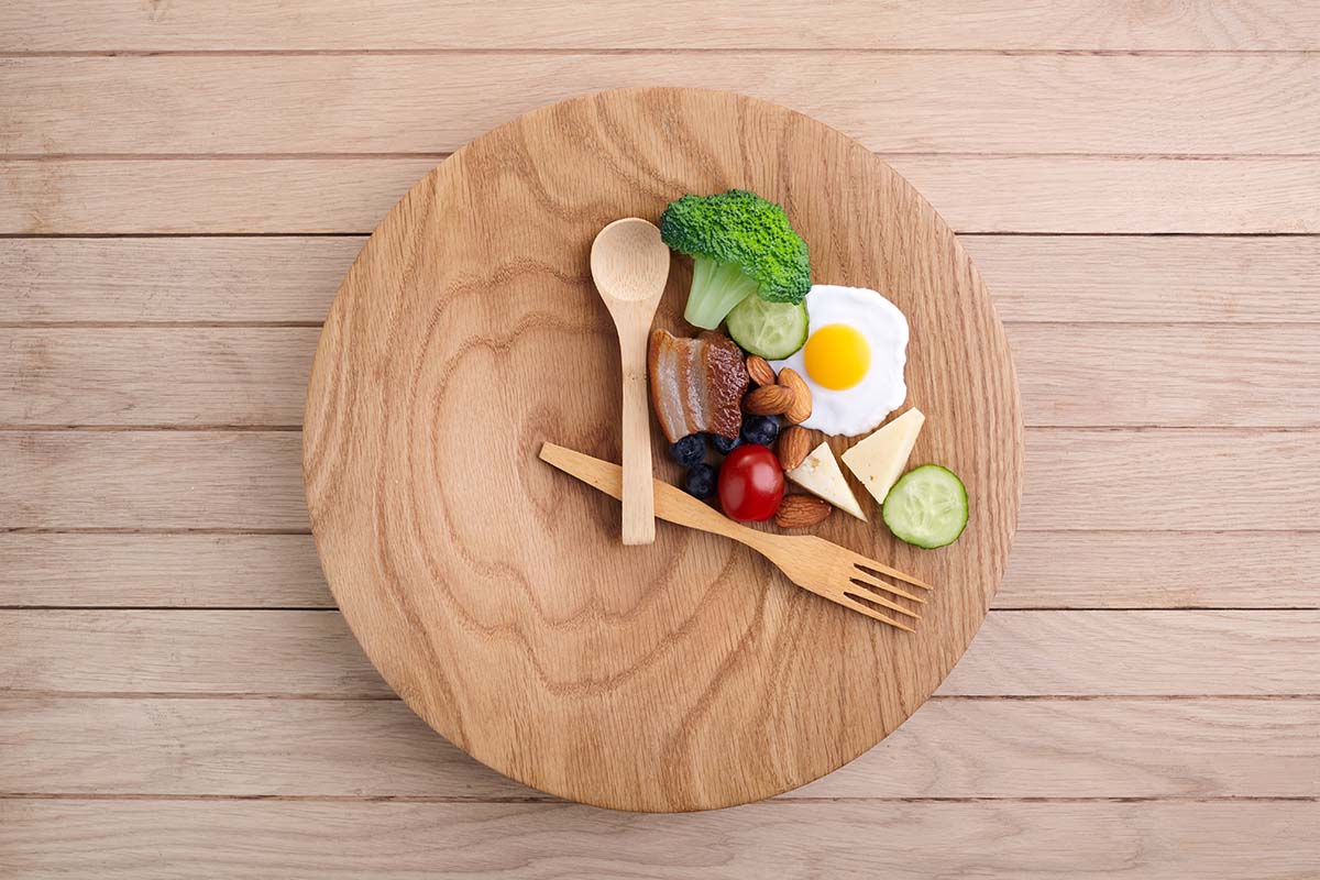 A wooden plate with wooden utensils set at 12 and 4 o’clock, healthy food is in the space between the utensils creating a portion that covers one third of the plate.