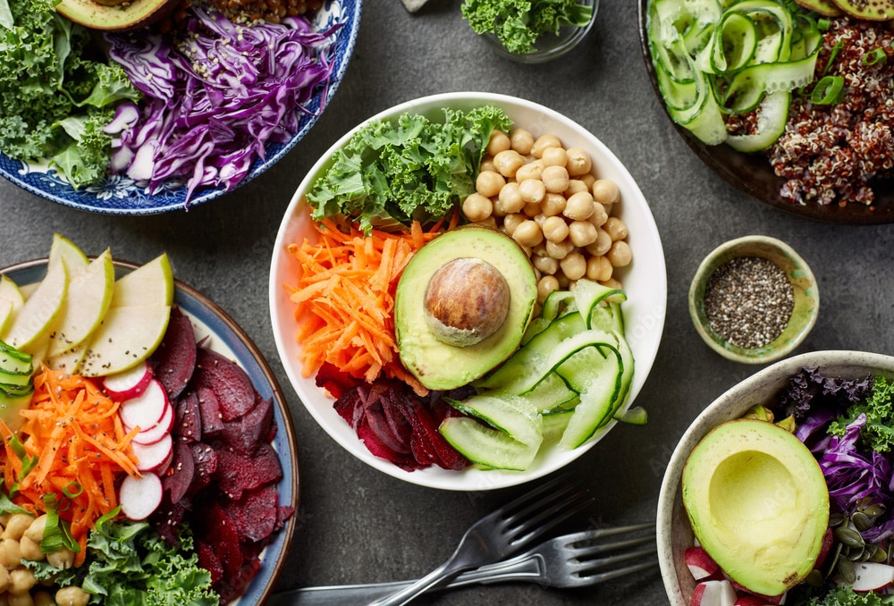 Several bowls of vegan meals consisting of kale, carrots, beets, avocado, chick peas, cucumber, radish, cabbage, and quinoa.