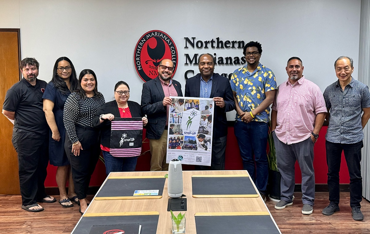 NIDDK leaders and Northern Marianas College staff stand next to each other in front of a white and red wall with the college’s logo on it.