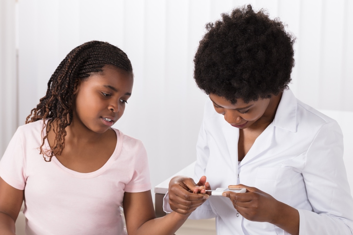  Woman helps her daughter check her glucose levels with a finger prick test.