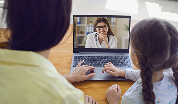 A mother and daughter on a telehealth video call with a doctor