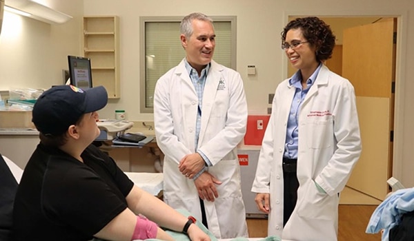 Two doctors talk with a study participant sitting in a hospital bed.