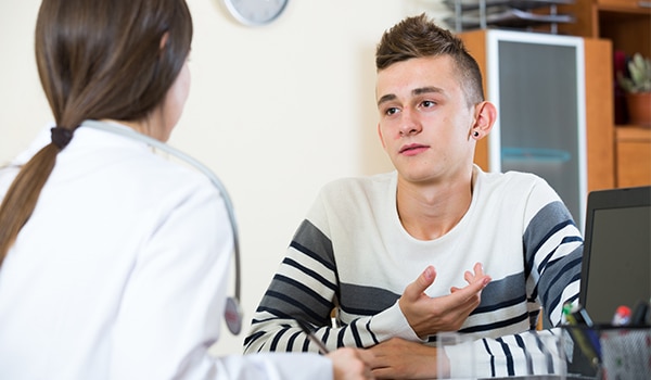 Image of a young female doctor sitting at a desk with her back to the viewer staring at an adolescent male patient.