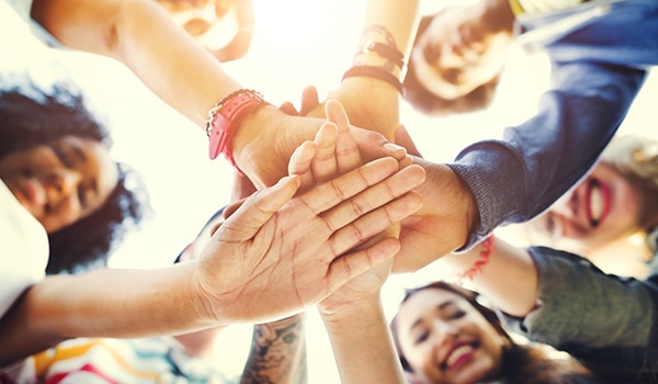 Image of adolescents stacking hands in a circle. The image focuses on the hands together with their faces blurred above the stacked hands.