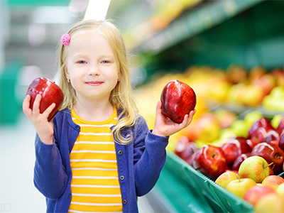A young girl holds two apples in her hands while at a grocery store.