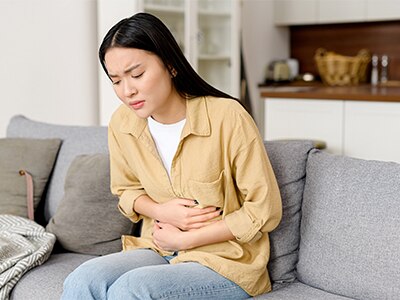 A person holding their stomach as if in pain while sitting at home.