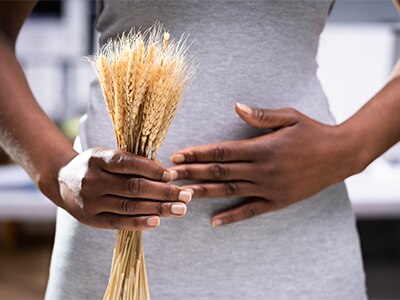 Person holding spikelet of wheat and their stomach, symbolizing celiac disease and gluten intolerance.