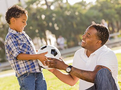 A father handing a soccer ball to a child.