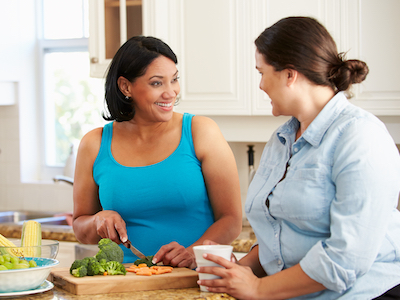 Two women in the kitchen talking and cutting vegetables.
