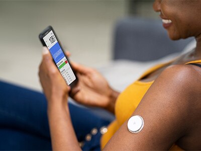 A person viewing information on their smartphone, tracking their blood glucose levels using a small sensor attached to the person's arm.