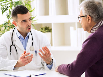 A male health care professional talking with an older man in an office.