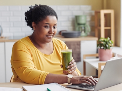 A woman using a laptop and drinking a smoothie.