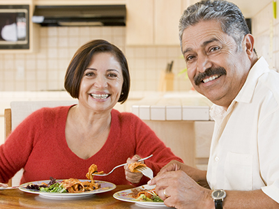 Man and woman eating pasta and salad at a kitchen table