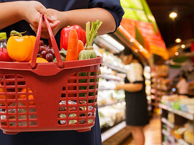 A person holding a grocery basket at a grocery store.