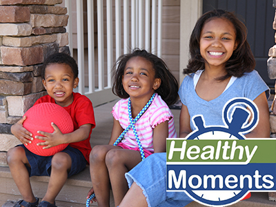 Young boy holding a ball, a young girl with a jump rope, and an older girl holding a watering can sitting on front porch