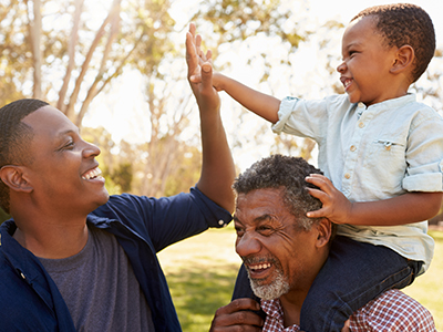 Father giving his young son, who is sitting on his grandfather's shoulders, a high-five