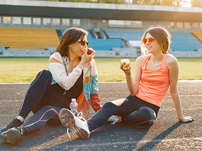Teenager and her mother eating apples while sitting outside after physical activity.