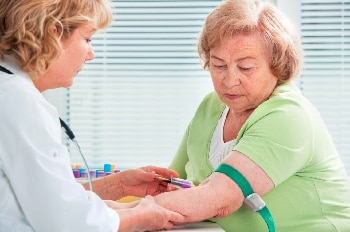 أخصائية رعاية صحية تسحب دم امرأة مسنة.