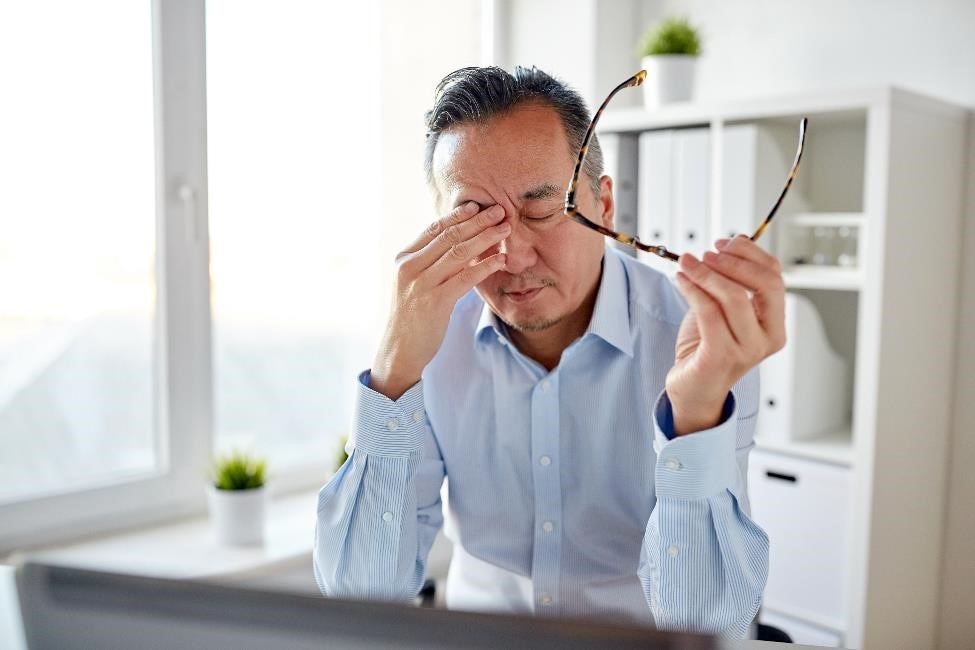A man rubbing his eyes while holding his eyeglasses.