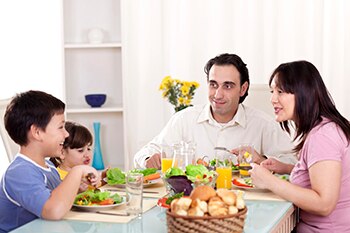 Una familia que está sentada alrededor de una mesa comiendo una comida saludable.