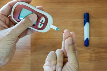 A pair of hands, one holding a blood glucose meter to pick up a drop of blood from a finger on the other hand.