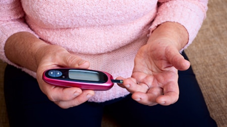 A woman holds a blood glucose testing meter next to a drop of blood on her finger.