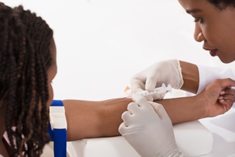 A health care professional draws blood from a patient’s arm.