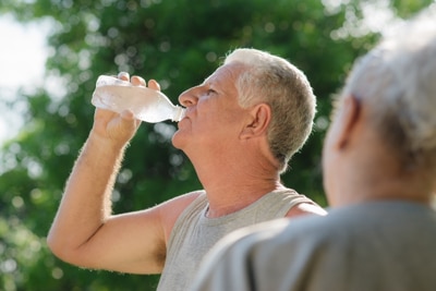 Photo of a man outdoors in exercise clothes drinking from a bottle of water.