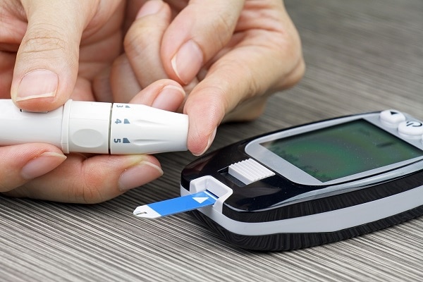 Photo of a woman's hands and a blood glucose meter. She is pricking her fingertup with a lancet.