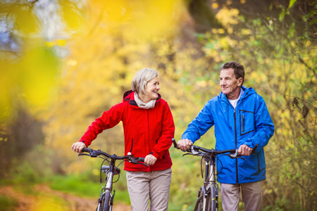A woman and a man walk their bikes through a park.
