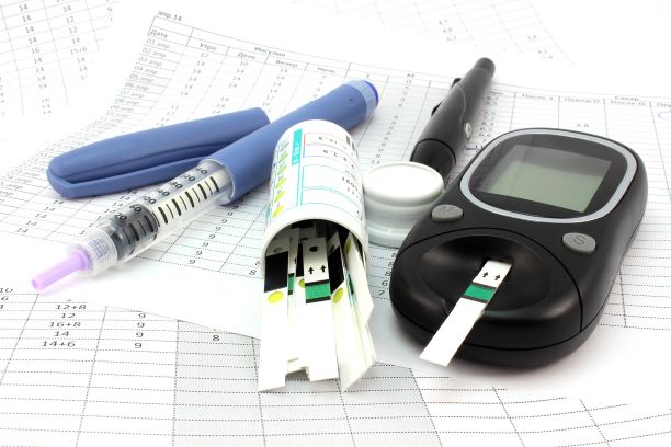 Diabetes supplies on a table, including a lancet, insulin syringe, glucose meter, and test strips.
