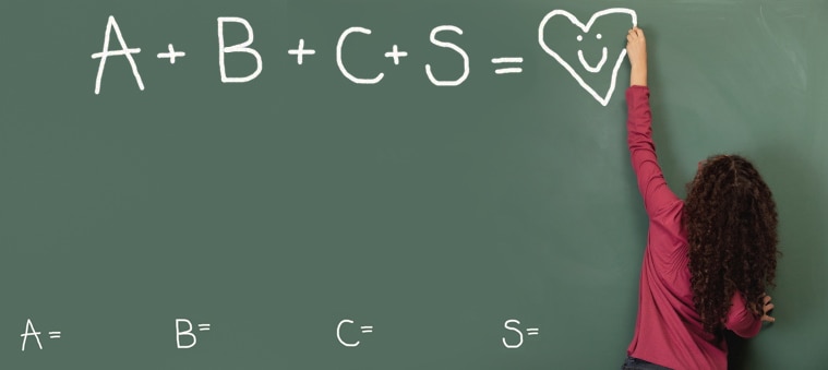Child writing “A+B+C+S = Heart” on a school chalkboard.