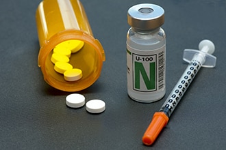 Diabetes medicines in a pill bottle, a vial of insulin, and a syringe.