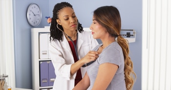 Health care professional listens to a woman’s heart with a stethoscope.