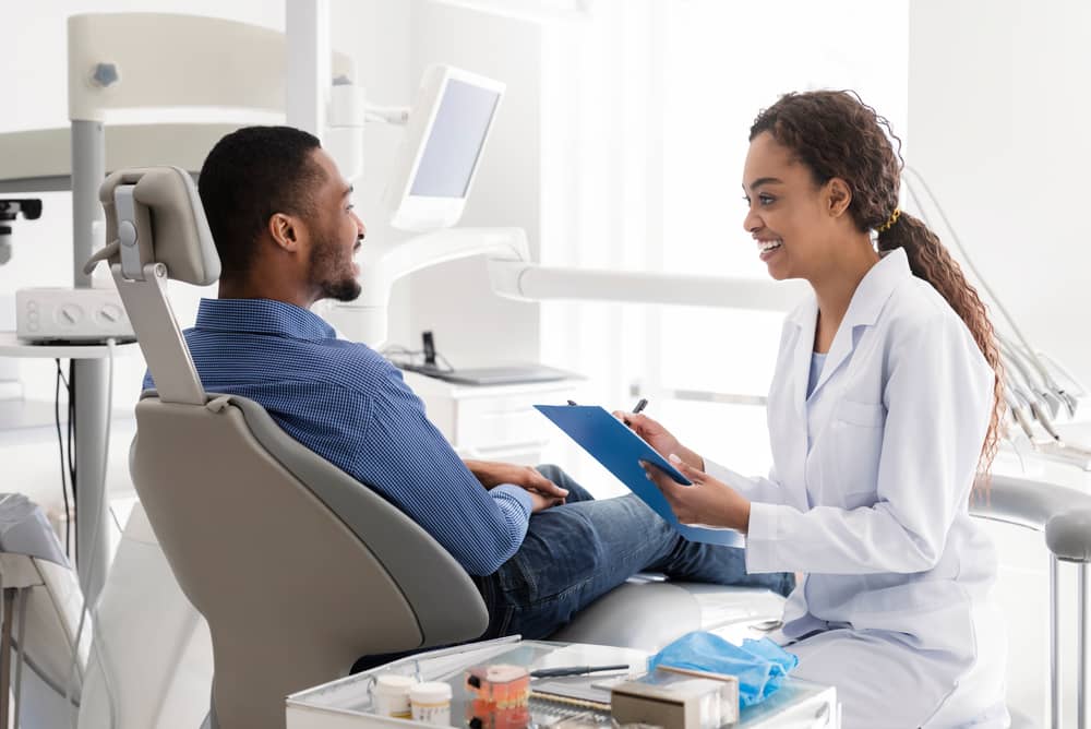 رجل جالس على كرسي أسنان يتحدث مع طبيب أسنان.